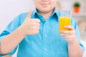 50835216 - healthy drink. chubby boy is holding a glass of orange juice and showing thumbs up.
