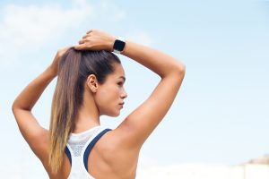 Lifestyle photo of young female on outdoor run adjusting hair showing product on arm